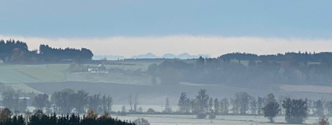 ein dunstiges Wiesental hinter dem schemenhaft chiemgauer Berge zu erahnen sind 