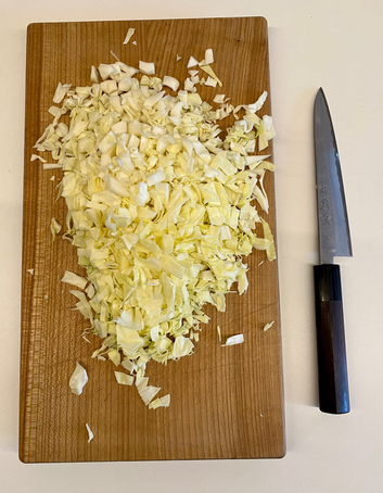 ein japanisches Messer liegt neben einem hölzernen Schneidbrett, auf dem ein Viertel Spitzkohl in kleinen Teilen liegt