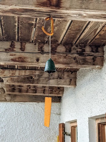 grünes Glöckchen hängt mit oranger Windfahne unter einem hölzernen Balkon 