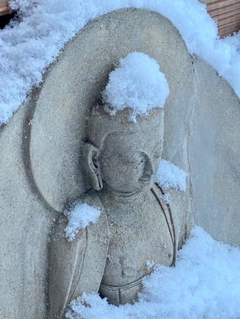 Schnee auf einer graubeigen kleinen Buddhastatue