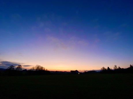 Sonnenuntergang mit orangem Streifen am Horizont und ein paar vereinzelten Miniwölkchen am blauen Himmel 