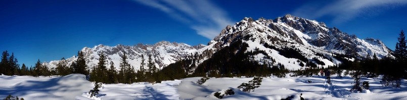 Blick über eine verschneite Fläche auf das Felsmassive von Steinernem Meer und Hochkönig nblauer Himmel mit 2 Streifchen Wölkchen