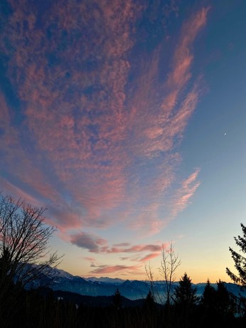 rosa Wolkenstreifen nach Sonnenuntergang an einem blauen Himmel und eine ganz dünne Mondsichel erschien
