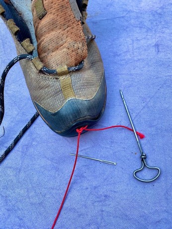 ein ausgelatschter Schuh, vor dem ein Handbohrer und eine Stopfnadel liegennnam Zehenschutz hängt eine verknotete rote Schnur