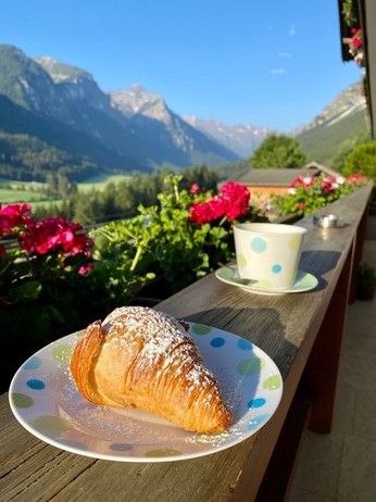 ein Croissant und ein Haferl Kaffee stehen auf der Balkonbrüstungnnim Hintergrund das Gschnitzral und die einrahmenden Berge