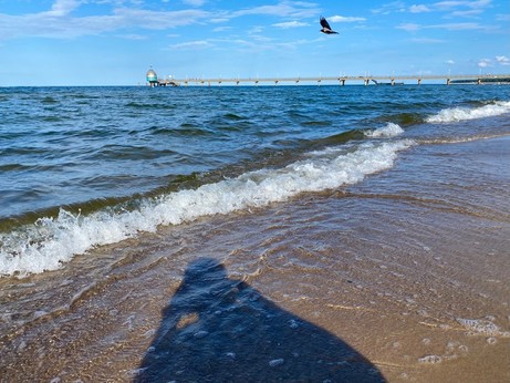 Meer, Wellen, Sand und eine Seebrücke im Hintergrund nSchatten des Fotografen im Vordergrund 