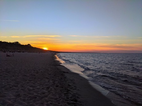 Sonnenuntergang am Meer mit orangem Streifen am Horizont und Sandstrand links und Meer rechts 