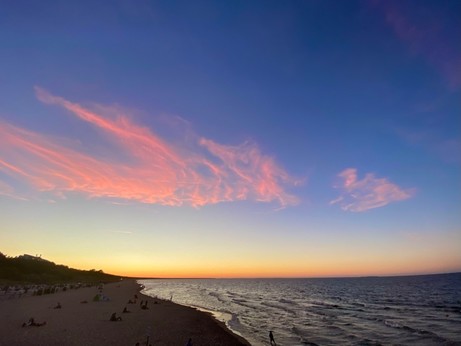 farbiger Sonnenuntergang über Meer und breitem Sandstrand und rosa Wölkchen am blauen Himmel 