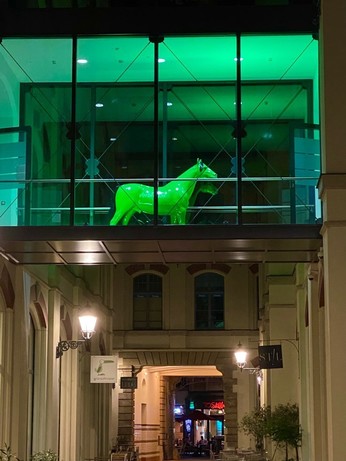 ein grünes Pferd steht in einem Übergang, der zwei Häuser verbindet 