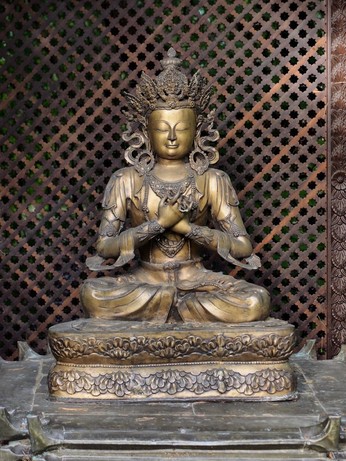 eine messingbronzefarbene Buddhastatue im Lotussitz mit überkreuzten Armen und geschlossenen Augen, lächelnd