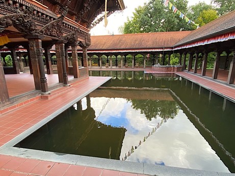 Säulenhalle rund um ein Wasserbecken, in dem sich eine lange Gebetsfahne spiegelt