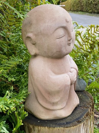 eine kleine Buddhafigur mit wallendem Gewand und übergroßem Kopf mit geschlossenen Augen schmunzelnd