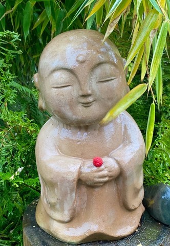 eine kleine stehende beige Buddhastatue mit einer kleinen Himbeere in den gefalteten Händen 