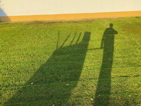 eine gemähter Rasen auf dem der Schatten von einem Mensch mit einem Handkarren zu sehen ist 