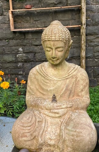 eine sitzende beige Buddhastatue hält eine viel viel kleinere Buddhafigur in ihren übereinander liegenden Händen 