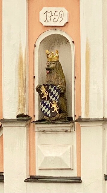 eine Figur eines braunen Bärs steht in einer Nische und hat eine Krone auf dem Kopf und hält ein Wappen nDie rosa Zunge ist erkennbar 