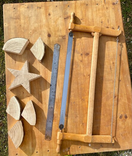 auf einem Holztisch liegen eine Gestellsäge und ein zugehöriges ausgetauschtes Sägeblatt und ein ausgesägter Holzstern und die Reststücke 