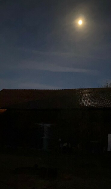 ein fahler Mond am Himmel und eine leichte Spiegelung im feuchten Dach der Scheune 