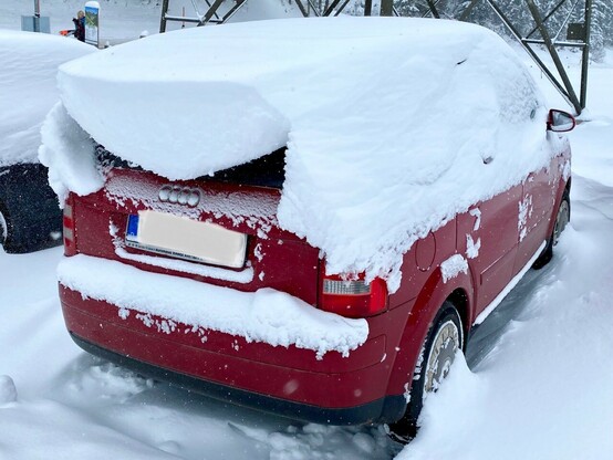 ein rotes Auto, an dessen Rückseite sich ein großer Schneeüberhang gebildet hat