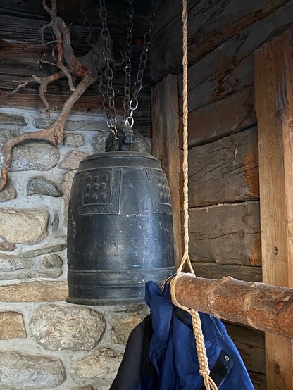 eine nicht kleine japanische Glocke und der Holzstab, um sie in Schwingung zu versetzen vor einer Natursteinwand und Holz