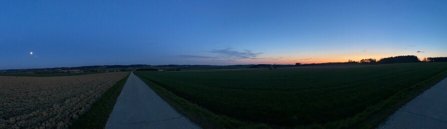 ein Panorama mit dem Vollmond am dunkelblauen Himmel links und den restlichen Farben nach einem Sonnenuntergang rechts 