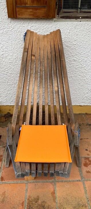 auf einem Stuhl, der nur aus Holzlatten zusammen geschnürt ist, liegt ein oranges Sitzkissen 