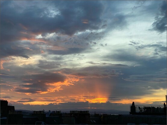 nach Sonnenuntergang leuchten ein paar orange Strahlen von unten durch die Wolken nach oben 
