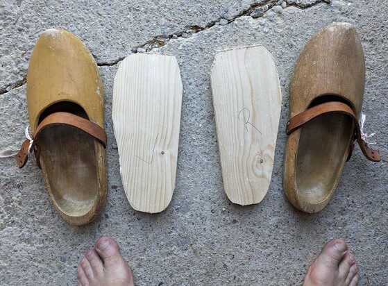 zwei Holzschuhe stehen außen neben zwei in ähnlicher Form der Schuhe gesägten Holzstücke