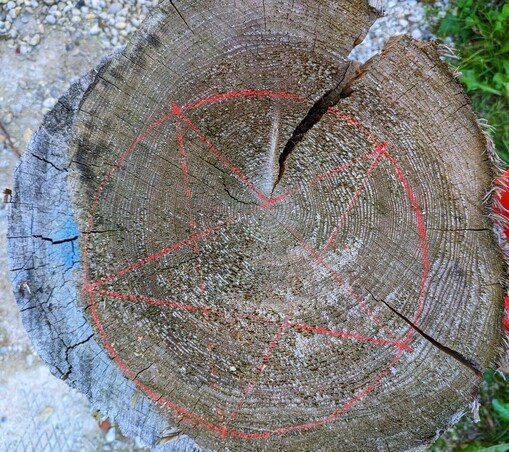 Auf einer gräulichen Holzscheibe ist ein roter fünfzackiger Stern in einem Kreis angezeichnet.