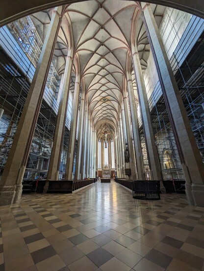 Der Blick von hinten durch ein sehr hohes Kirchenschiff mit einem Kreuzrippengewölbe. Im Boden ist ein Karomuster erkennbar.