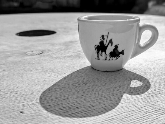 eine weiße Espressotasse mit der schwarzen Silhouette von dem langen dürren Ritter Quijote zu Pferd und mit Lanze und seinem kleinen Begleiter Sancho Panza auf dem Esel auf einer weißen Tischplatte