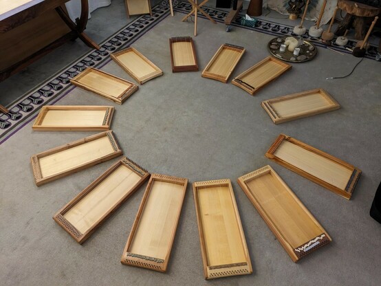 13 Monochorde aus verschiedenen Holzarten liegen im Kreis auf einem eher grauen Teppich