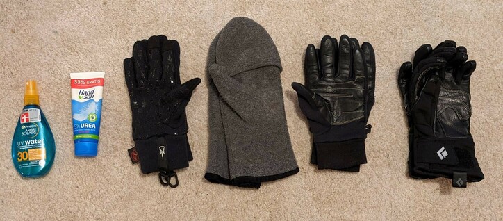 vier unterschiedliche Paar Handschuhe liegen auf einem beigen Teppich. Daneben Sonnenschutz und Handcreme