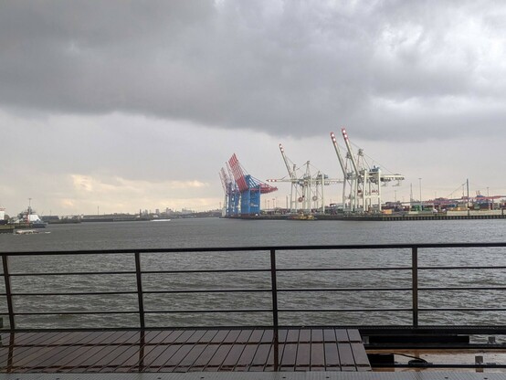 Blick übers Wasser auf hochgeklappte Kräne zur Be/Entladung von Containerschiffen