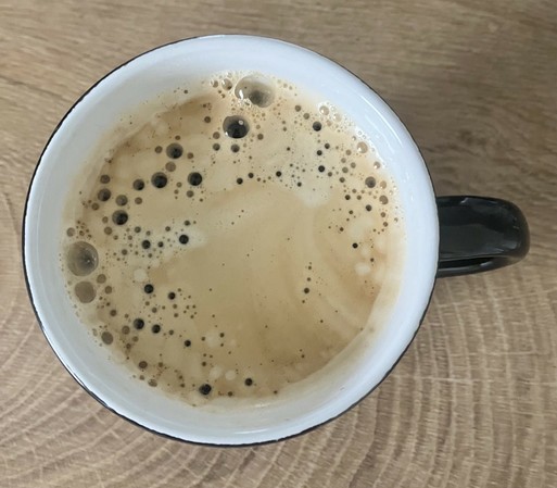 Kaffeetasse mit weißem Rand innen und schwarzem Henkel außen, von oben fotografiert, Kaffee ist schwarz, aber cremig.