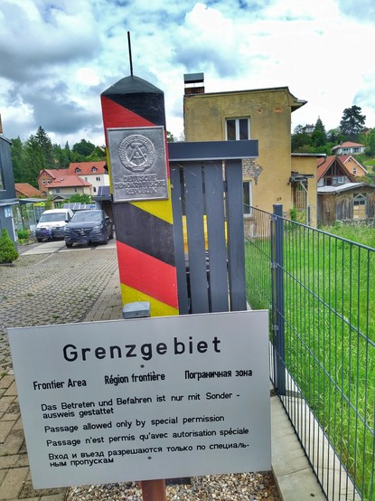 An einem Privatgrundstück ein nachempfundener Grenzpfosten der DDR mit Schild: Grenzgebiet in dei Sprachen