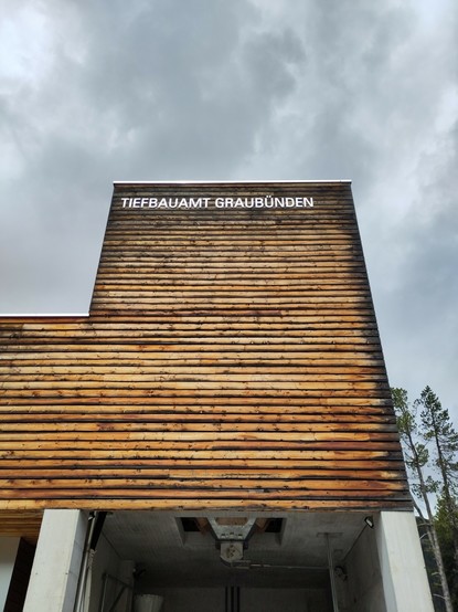 Foto. Ein Gebäude mit Holzfassade und Aufschrift TIEFBAUAMT GRAUBÜNDEN.