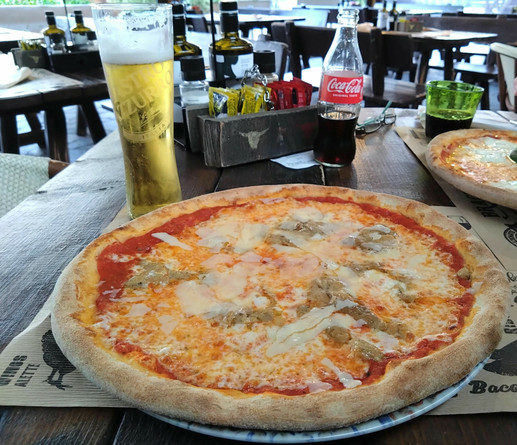 Große Pizza und ein Bier auf einem Tisch auf einer Terrasse.