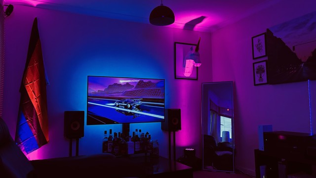 my living room bathed in cyan and magenta light, showing some retro-style low-poly animation of a matching colour scheme on the TV, next to my low-poly unicorn head that is protruding from a picture frame on my wall
