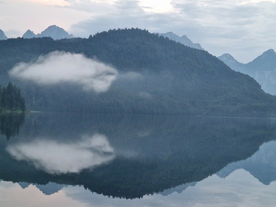Sich in einem See spiegelnde Berge und eine tiefe Wolke.