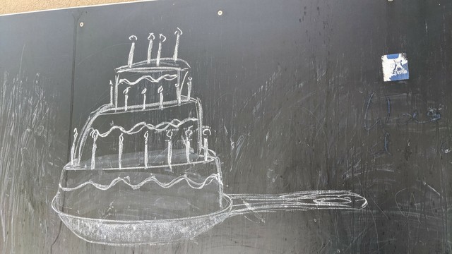 Kreide auf Tafel, gemalt auf einem Spielplatz, alles in weiß 

Ein mehrstöckige Torte mit Kerzen.
In einer Bratpfanne 