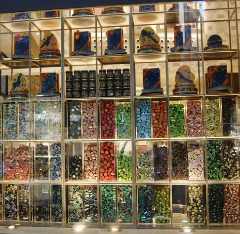 Ein Schaufenster mit einer Vielzahl von bunten verpackten Pralinen, die in einem Raster aus durchsichtigen Fächern angeordnet sind. Die oberen Regale sind mit dekorativen Schachteln und Dosen ausgestattet.