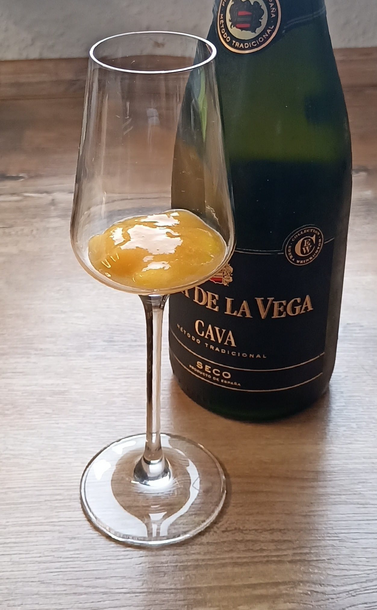 Eine Flasche Sekt Finca de la Vega Cava 
Davor steht ein Sektglas, in dem schon das Pfirsichpüree auf den Sekt wartet.