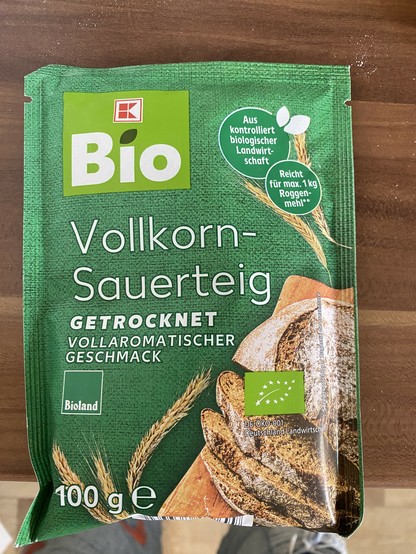 Eine Packung getrockneter Bio-Vollkornsauerteig, grüne Verpackung, mit einem Brot und Ähren eines Getreides. 