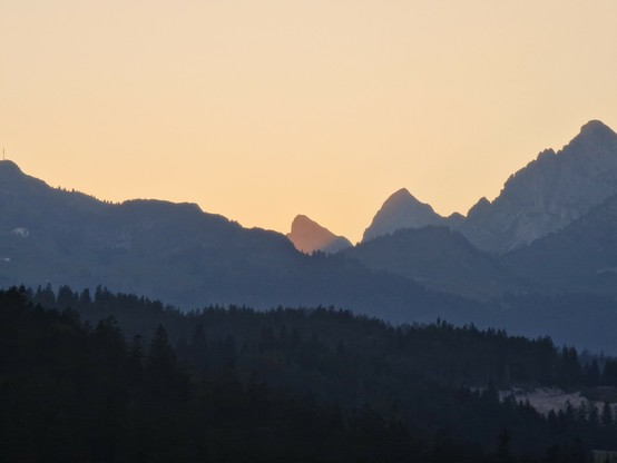 Silhouette einer Bergkette in der Abenddämmerung. Nur ein Gipfel wird noch von der Sonne beschienen.