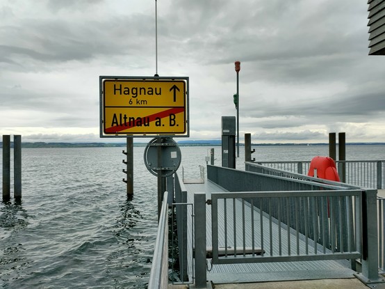 Deutsches Ortsschild am Steg der Schweizer Schiffstation Altnau am Bodensee in Richtung Hagnau über den See.