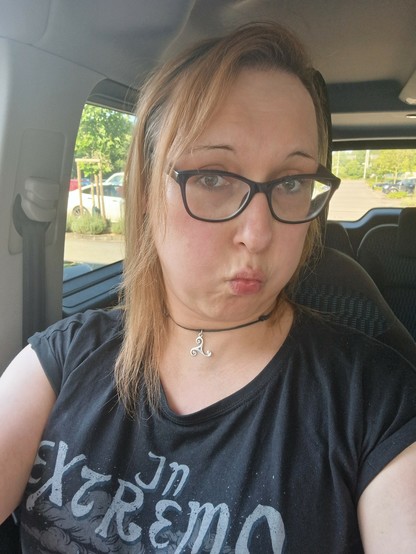 Selfie einer Frau, ich,  mit großer Brille und kupferroten Haaren.  Sie sitzt im Auto und hat die Backen aufgebläht, als würde sie gleich explodieren und ihre Wangen sind deutlich gerötet.