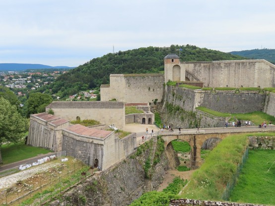 Foto: Festung über mehrere Ebenden mit dicken Mauern und Türmchen, dahinter ein grüner Hügel