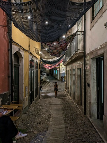 eine enge Gasse nachts in der Altstadt von Coimbra und zwischen den Häusern sind gehäkelte Tücher gespannt 