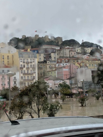 grauer Himmel nunscharfe Regentropfen an der Scheibe und dahinter die Altstadt und Burg von Lissabon 